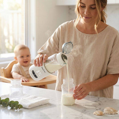 Australian mum pouring warm milk from the Babycozidoo Portable Bottle Warmer into a baby bottle, smiling baby in highchair behind, sunlit marble kitchen